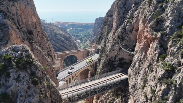 Ascending drone shot revealing Mascarat Canyon and its three bridges with traffic