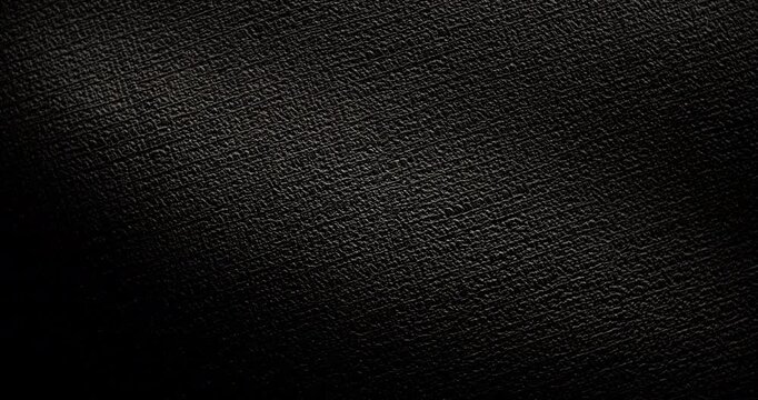 Seamless Abstract black texture.  A slow, smooth loop rotation of a dark, rough surface, gently rotating under the light, creating subtle highlights.