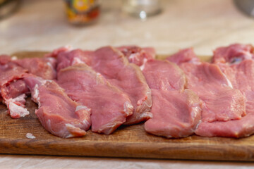 Fototapeta premium Raw meat slices on a rustic wooden cutting board. Fresh pork or beef fillets prepared for cooking a traditional homemade meal.