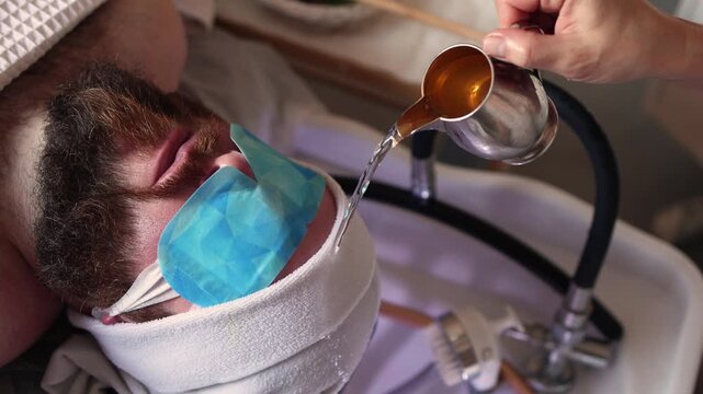 Cosmetologist Pouring Water from Golden Pitcher Over Bearded Man with Blue Eye Patches and Hot Towel Wrap During Luxury Japanese Head Spa Treatment, Relaxing Male Scalp Ritual with Purple Ambient Ligh