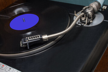 A vintage vinyl record player with a record mounted on it. Platter holding the record, the tonearm with the cartridge and stylus. Vinyl record with an unmarked blue sticker. 33 revolutions per min.  © miraleks