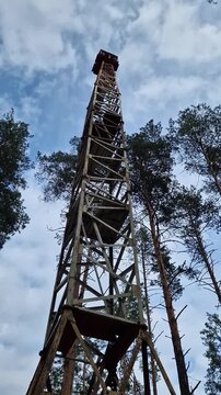 Old fire watchtower in the forest against a blue sky. High metal structure of an abandoned forest tower, shot from a lower perspective. Rusty steel tower with an observation deck on top