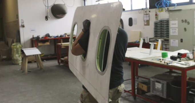 Person carrying a large curved metal airplane panel through an industrial workshop