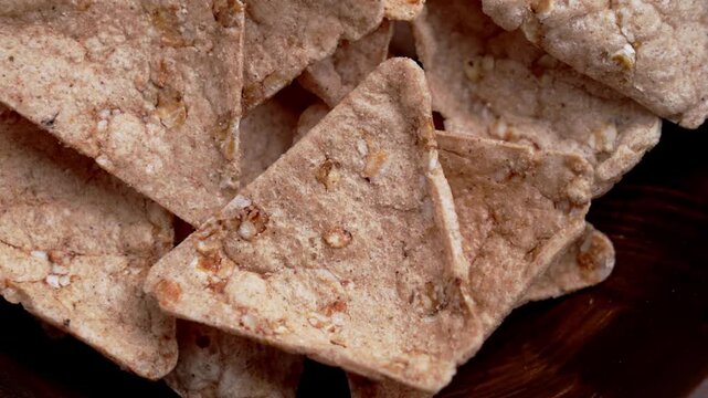 Dietary organic buckwheat nacho falling into a wooden bowl. Triangular brown crackers.
