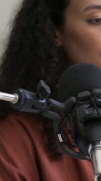 Vertical video: Host in rust top leaning to mic in studio as camera rolls reading notes, copy space