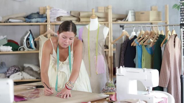 Using curve ruler, woman tailor draws dress diagram scheme on paper. Craftsman creates pattern for making dress. Creating prototype of product on paper, staff draws pattern
