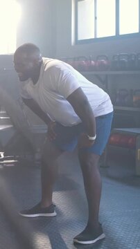 Vertical video: Rope training man in shorts doing rope waves and bracing thighs at gym, kettlebells