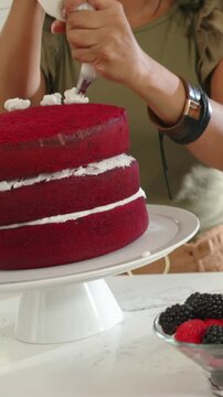 Home baker baking positioning piping bag and squeezing rosettes around cake for neat decoration