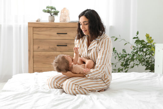 Happy mother with her little baby sitting on bed at home