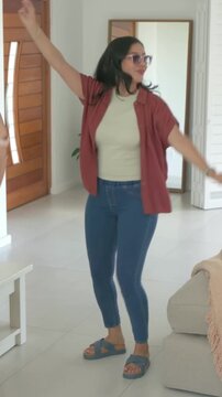 Vertical video: Putting on sunglasses, women dancing around coffee table at home for fun with phone