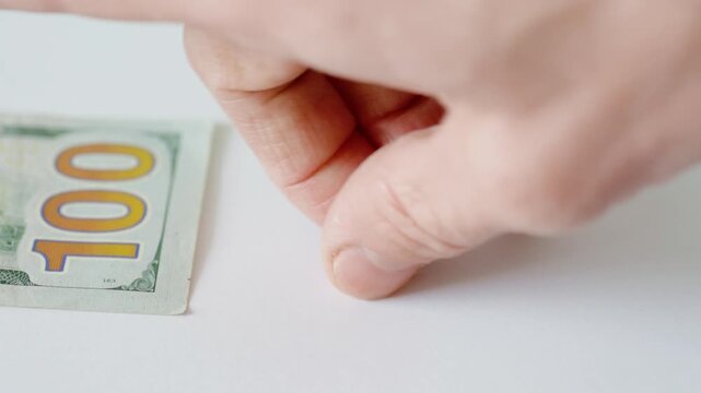 Elderly white hands carefully inspect hundred for authenticity on bright white table, fingertip rubs security features and ink, clinical closeup showing skin texture and methodical
