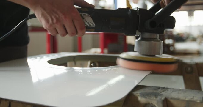 Worker using an electric orbital sander to polish the surface of a white circular metal part