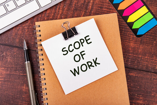 Scope of Work text on a white note paper clipped to a spiral notebook on a wooden desk. Business concept for project planning, contracts, and management.