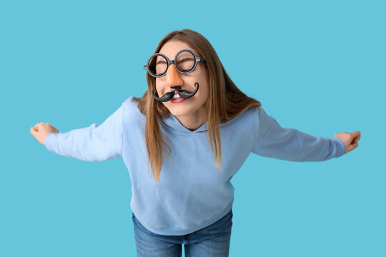 Beautiful young happy woman in funny disguise on blue background. April Fools Day celebration