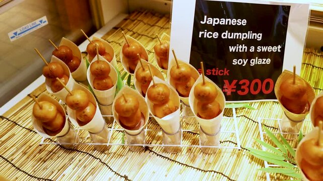 Japanese rice dumplings on sticks with sweet soy glaze served in paper cones at a food stall.