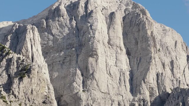 Aerial view of the stark, textured face of a mountain, etched with deep crevices under a blue sky, Teth, Shkoder County, Albania.