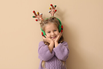 Happy little girl in reindeer antlers and earmuffs on beige background © Pixel-Shot