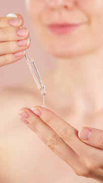 Young woman holding a dropper with serum for face. Macro view pink background. Dermatology, cosmetics, spa ads. Liquid collagen skincare product, beauty concept. Facial oil fall from a glass pipette 