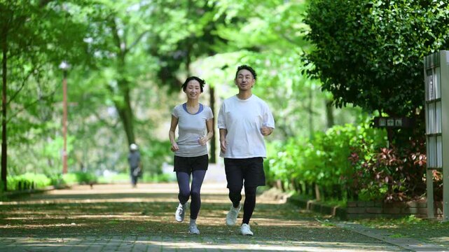 新緑の公園でウォーキングやランニングのスポーツが楽しいミドル夫婦の正面　健康的（ヘルスケア）ライフスタイルのイメージ全身の動画半袖
