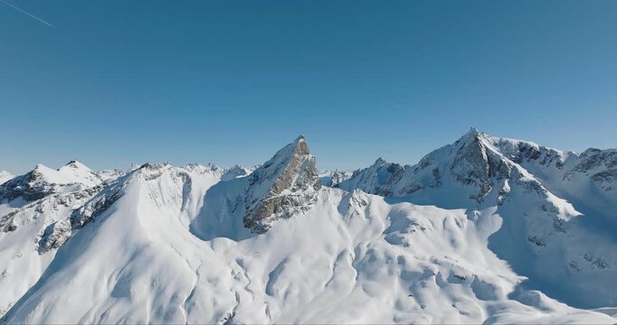Aerial view of majestic snow-covered mountain peaks under a clear blue sky, creating a striking contrast of white and blue, Lech, Vorarlberg, Austria.