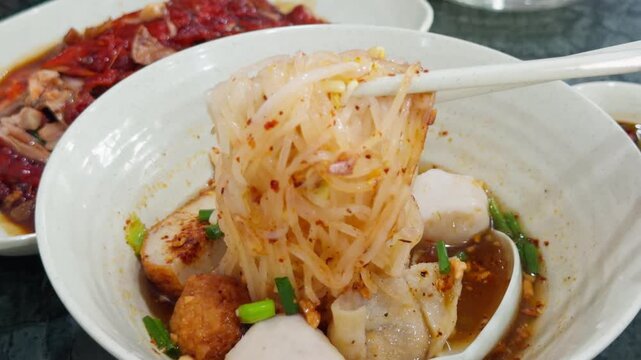 Chopsticks Lifting Noodles from Thai White Broth Soup Bowl - Asian Rice Noodle Seafood Soup Close Up