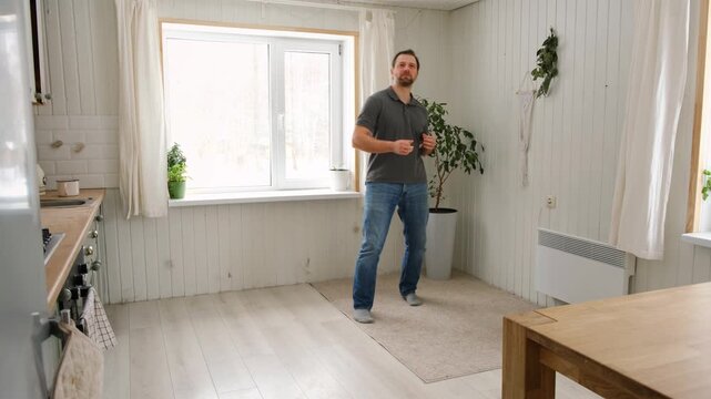 Handsome bearded man dance, have fun at home listens song, moves to music, feels overjoyed, celebrate good news, relish carefree life looks happy. Young adult male twirls, grooves, dancing in kitchen