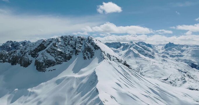 Aerial view of snow covered mountains, with blue sky and white clouds, creating a stunning winter landscape, Arlberg, Austria.