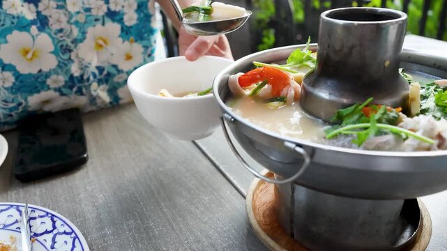 Serving Traditional Thai Tom Yum Seafood Soup from a Metal Hot Pot