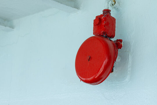A vibrant red emergency alarm bell is mounted on a light-painted wall, commonly used on ships, in factories, and commercial buildings as a visible and reliable safety alert system.