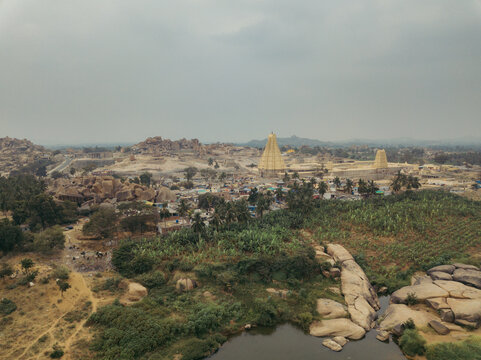Aerial view of striking temples piercing the horizon amidst a landscape of ancient ruins and vibrant greenery, Hampi, Karnataka, India.