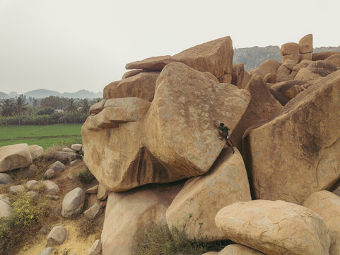 Aerial view of weathered boulders cascading across the landscape, contrasting with the verdant fields stretching towards the horizon, Hampi, Karnataka, India.