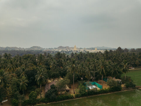 Aerial view of lush canopies contrasting with the ancient temples of Hampi under a blanket of grey sky, Hampi, Karnataka, India.