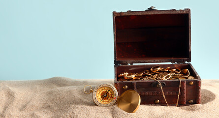 Old chest with treasures and compass on sand against blue background © Pixel-Shot