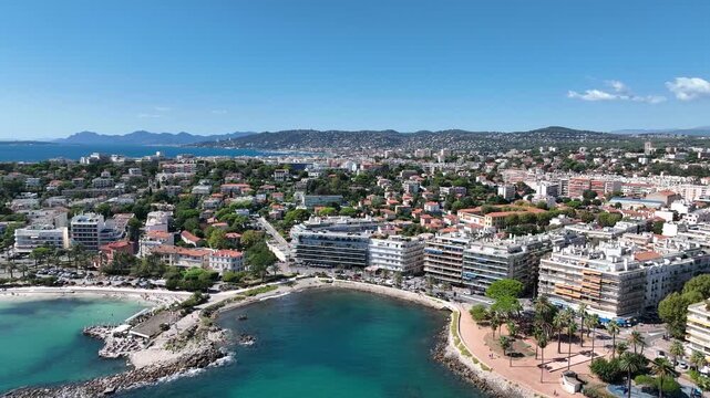 Aerial view of the beach with a mix of buildings, trees, and blue water, creating a vibrant and contrasting scene, Antibes, France.