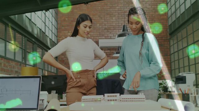 Two designers examining model in loft, right pointing, green overlay marking parts, refining plan
