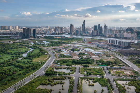 Aerial view of a modern skyline pierced by skyscrapers beyond a landscape of green spaces and developing plots, Ho Chi Minh City, Vietnam.