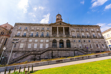 Obraz premium Impressive historic building of Palacio da Bolsa with clock tower and grand staircase in Porto city center. Elegant architecture, people relaxing in park and sunny European urban atmosphere.