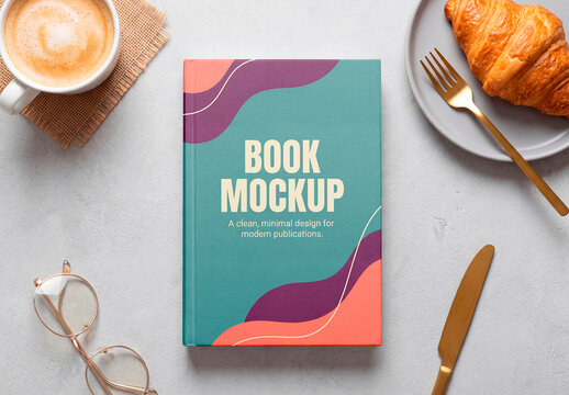 Blank hardcover book mockup with coffee and croissant breakfast scene