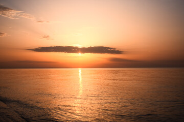 Fototapeta premium sun sets over ocean, creating radiant glow that stretches across water surface. horizon glows with soft orange and yellow tones, providing peaceful scene. stunning sunset with sun dipping into sea,