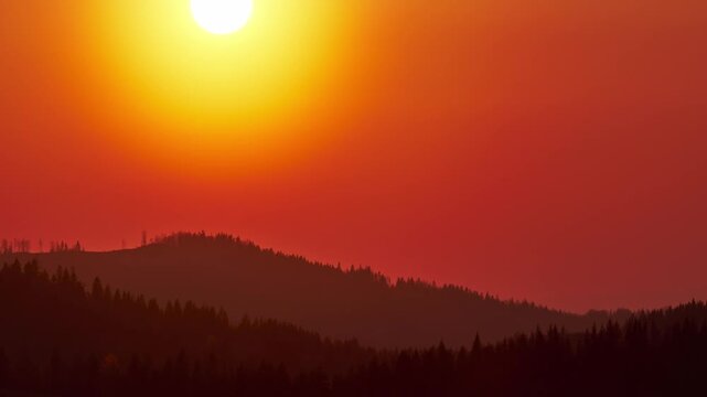 Cinematic time lapse of vibrant red sunset over mountain forest silhouette