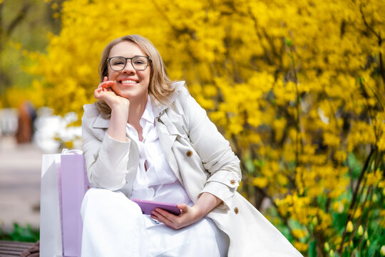 Smiling woman sitting on bench with smartphone. Happy spring lifestyle and relaxation.