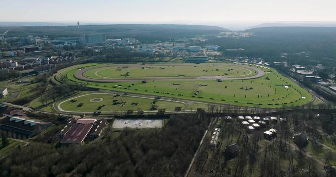Aerial view of a lush green race track surrounded by a dense forest and buildings, creating a striking contrast, Nancy, France.