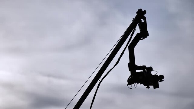 Camera crane jib with professional video camera against cloudy sky during production
