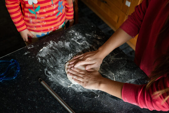 Hands of teenager stretching out pastry with flour underneath, helping her sister