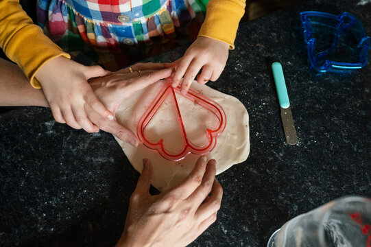 Hands of child and mother using a heart shaped cookie cutter on pastry