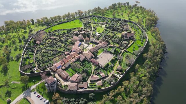Drone circular view around Granadilla medieval village in Spain, showing fortified walls, rooftops and surrounding reservoir landscape from above.