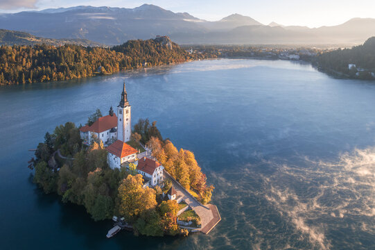 Aerial view of Lake Bled's island church bathed in the soft morning light, with a delicate mist rising from the water's surface, Bled, Radovljica, Slovenia.
