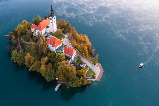Aerial view of the iconic Church of Mary the Queen, standing proudly on Bled Island, its white walls contrasting with the autumn foliage, Bled, Radovljica, Slovenia.