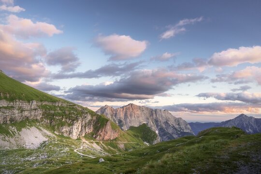 Aerial view of the rugged mountain peaks kissed by the soft glow of the setting sun, casting shadows over the green slopes, Log pod Mangartom, Bovec, Slovenia.
