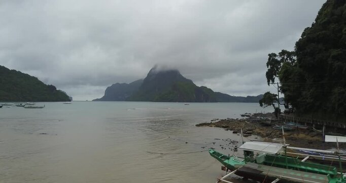 Low altitude aerial view flying forward over tropical bay with traditional boats and limestone island in El Nido, Palawan, Philippines